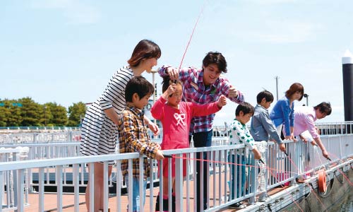 晴天の下、桟橋で釣りを楽しむ家族連れや子ども達